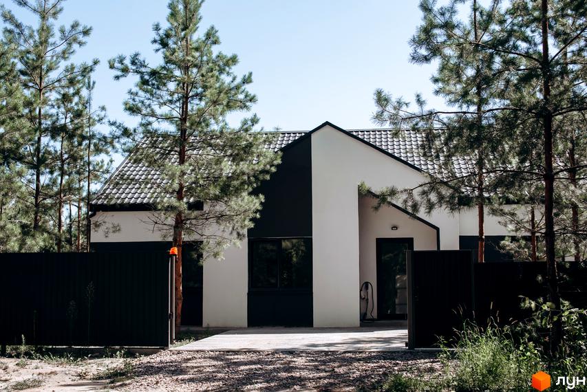 Котеджне містечко Chaletville: двоповерховий будинок з біло-чорним фасадом та черепичним дахом, оточений соснами та огороджений парканом.