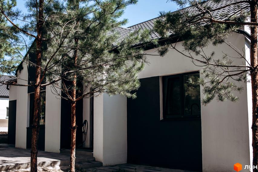 Котеджне містечко Chaletville: фасади будинків з білими та чорними елементами, вікна, дах, дерева та бруківка.