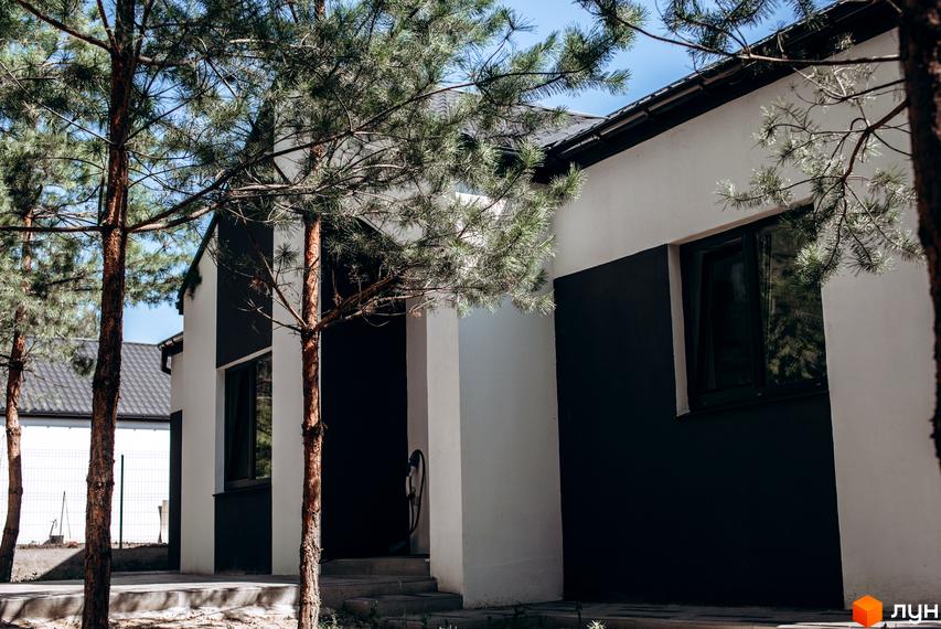 Котеджне містечко КМ Chaletville. Зовнішній вигляд будинку з чорно-білим фасадом та вікном, оточений деревами.