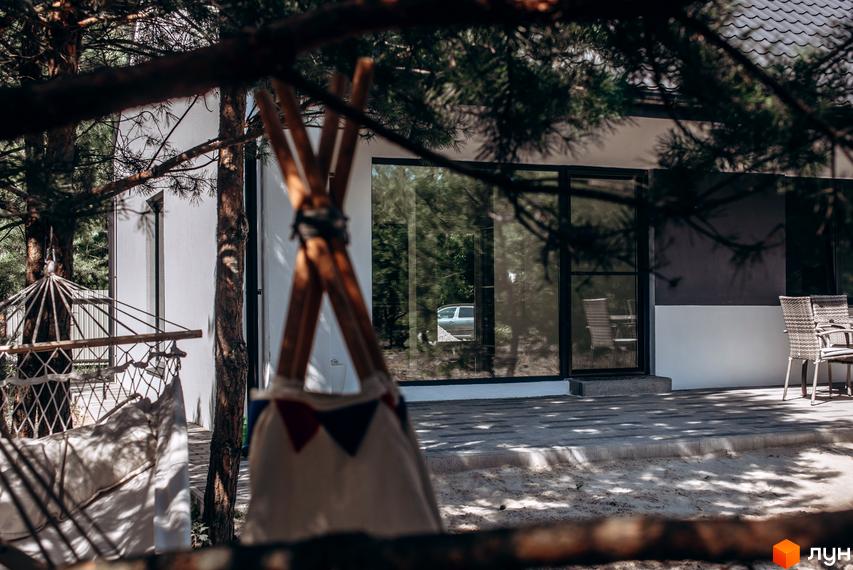 Котеджне містечко Chaletville: білий будинок з великими вікнами та терасою, поруч гамак та дитячий намет.