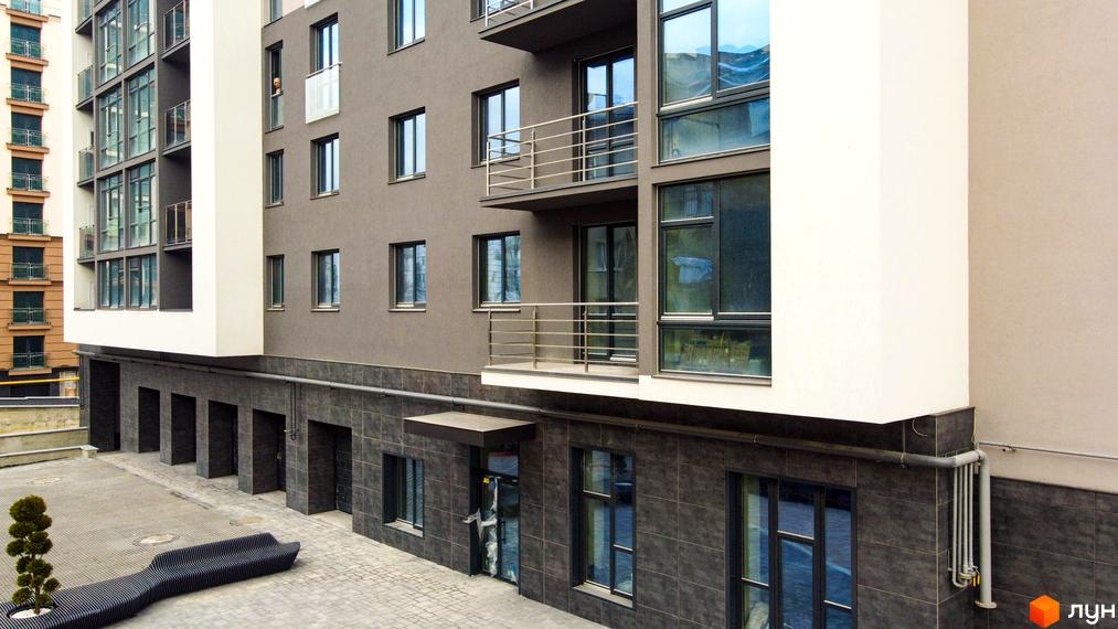 Зовнішній вигляд новобудови Park Residence з балконами та вікнами. Прибудинкова територія з лавою та деревом.
