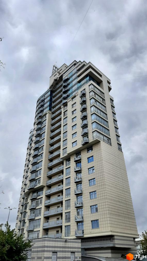 Зовнішній вигляд житлового комплексу Парус: висотна будівля з балконами та скляними фасадами на фоні хмарного неба.