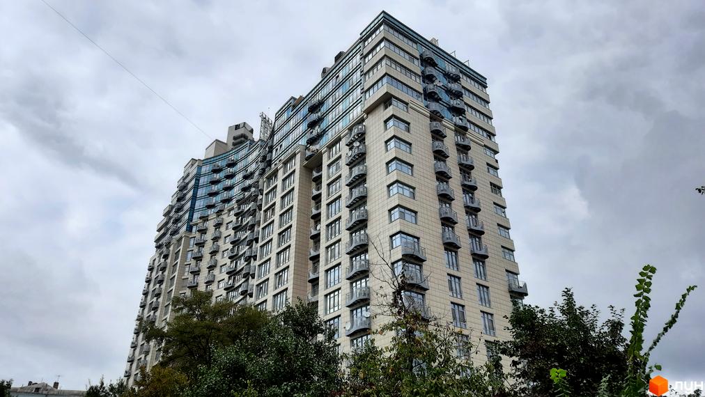 Житловий комплекс Парус - висотна новобудова з численними балконами та скляними фасадами на тлі хмарного неба. Навколо будівлі видно зелені дерева.