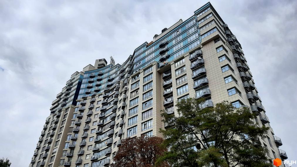 Зовнішній вигляд житлового комплексу Парус з вигнутим фасадом та численними балконами на тлі хмарного неба. Новобудова має сучасний дизайн та виглядає вражаюче.