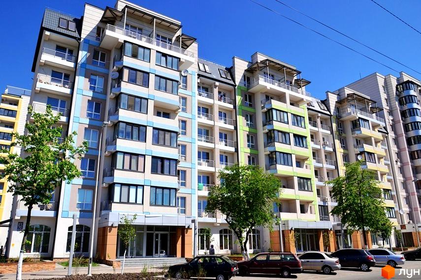 Житловий комплекс Акварелі: багатоповерхові будинки з кольоровими фасадами (блакитний, зелений) та великими вікнами. Прибудинкова територія з деревами та припаркованими автомобілями.