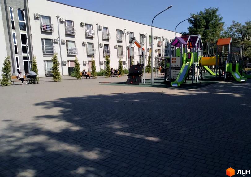 Зображення Житлового комплексу Золоті Стовпи з дитячим майданчиком та лавками для відпочинку. Світла будівля з балконами.