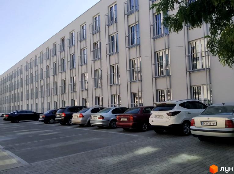 Зображення фасаду Житлового комплексу Золоті Стовпи з парковкою. На фото видно багато автомобілів, що припарковані біля будівлі.