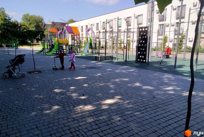 Зображення дитячого майданчика у Житловому комплексі Золоті Стовпи. На фоні видно багатоповерховий будинок з великою кількістю вікон.