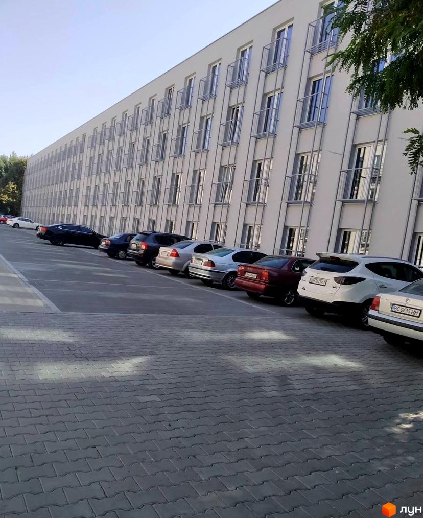 Зображення фасаду Житлового комплексу Золоті Стовпи та парковки. Багатоповерхова будівля з великою кількістю вікон та балконів.