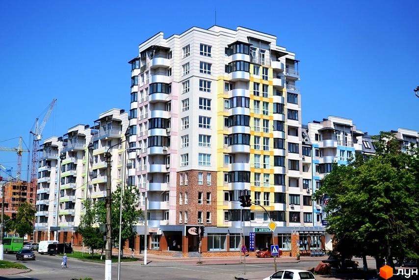 Житловий комплекс Акварелі з багатосекційними будинками світлих відтінків з кольоровими балконами. Вигляд на новобудову з вулиці з деревами та дорожнім рухом.