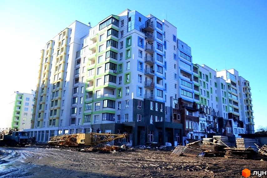 Житловий комплекс Акварелі з фасадами у світлих відтінках жовтого, зеленого та синього. На передньому плані видно будівельний майданчик з технікою та матеріалами.