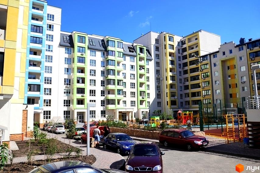 Житловий комплекс Акварелі: багатоповерхові будинки з яскравими фасадами та прибудинкова територія з парковкою і дитячим майданчиком.