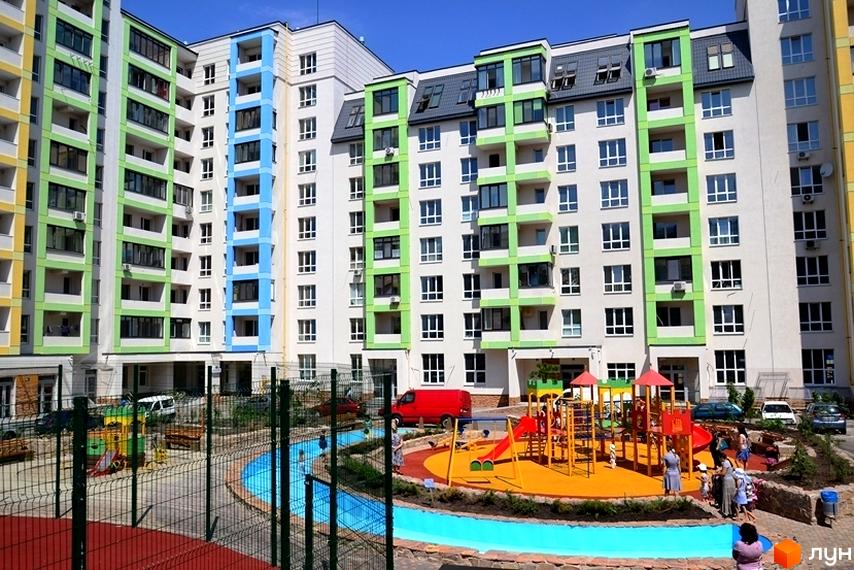 Багатоповерхові будинки Житлового комплексу Акварелі з білими фасадами та яскравими кольоровими балконами. На передньому плані облаштований дитячий майданчик.