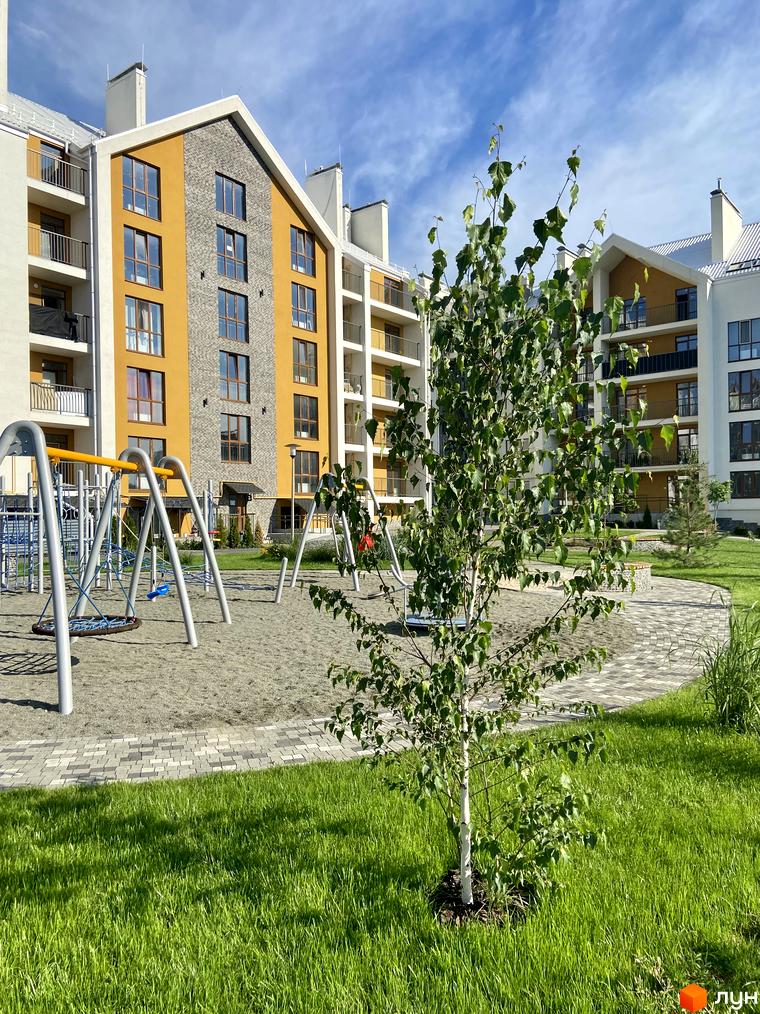 Житловий комплекс Гостомель Residence з жовто-сірими фасадами та білими дахами. На передньому плані дитячий майданчик та зелений газон.