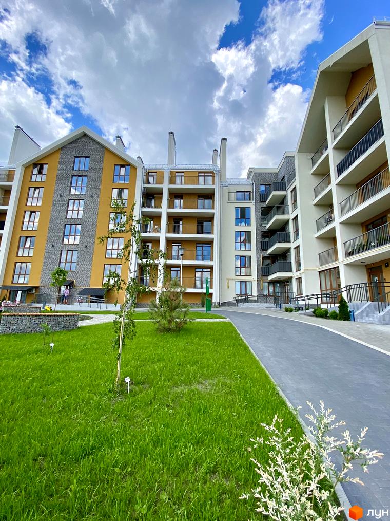 Зовнішній вигляд житлового комплексу Гостомель Residence з балконами та великими вікнами. На передньому плані зелений газон та пішохідна доріжка.