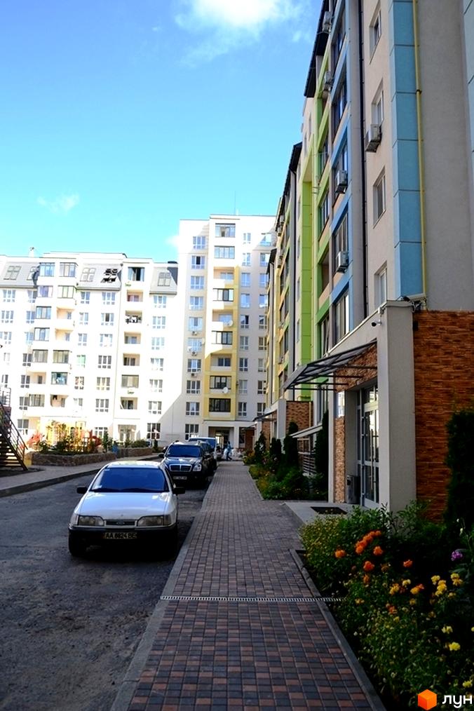 Житловий комплекс Акварелі: багатоповерхові будинки з кольоровими фасадами, брукований тротуар та клумби з квітами.