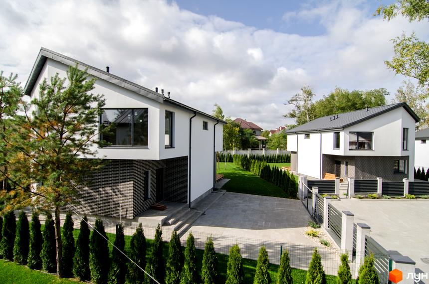 Котеджне містечко КМ Friends Club з білими фасадами та цегляною обробкою, огороджена територія з газоном та туями.