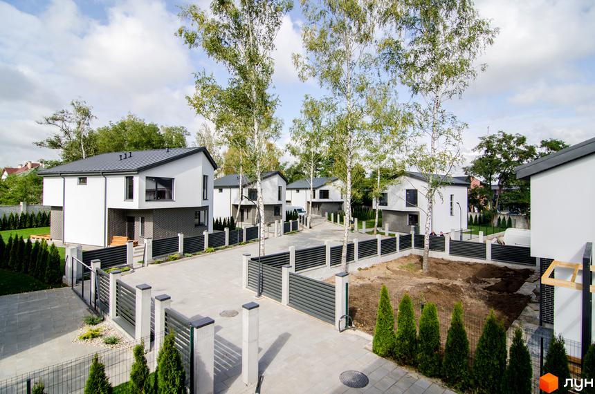 Білі будинки з темними дахами в Котеджному містечку Friends Club. На території є дерева, газон та огорожа.