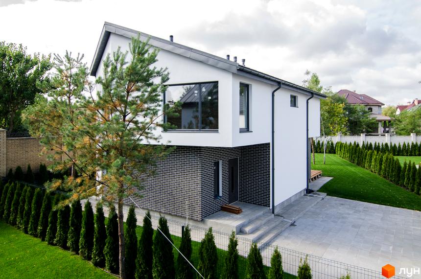 Котеджне містечко КМ Friends Club: двоповерховий білий будинок з цегляним цоколем та великим вікном, доглянута зелена галявина з туями.