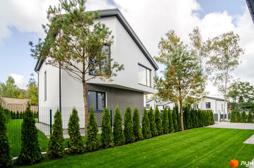 Котеджне містечко КМ Friends Club. Зовнішній вигляд білого двоповерхового будинку з цегляною обробкою, зелений газон та туї на прибудинковій території.