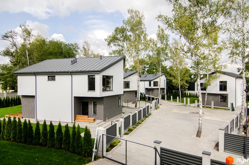 Білі будинки з сірими дахами та фасадами з цегли в котеджному містечку Friends Club. На території є дерева, газон та паркан.