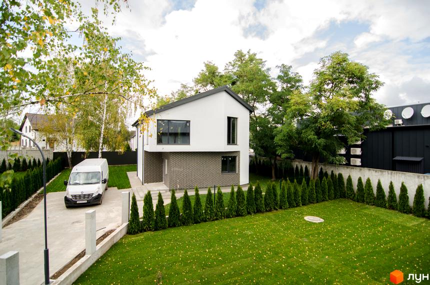 Двоповерховий будинок з білими стінами та темно-сірим дахом. Перед будинком газон та ряд туй, що створюють затишну атмосферу в Містечку котеджів Friends Club.