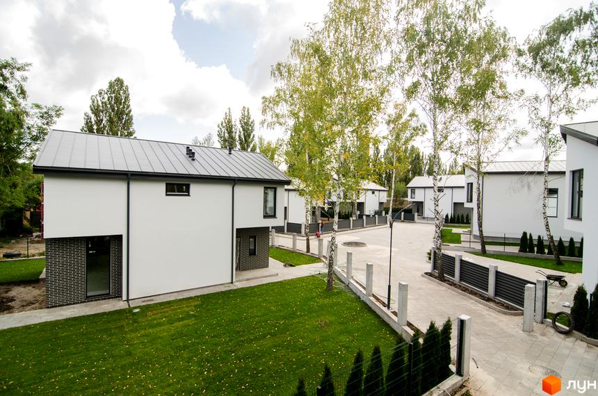 Котеджне містечко КМ Friends Club. Зовнішній вигляд білих двоповерхових будинків з металевими дахами та прибудинкова територія з газоном та деревами.