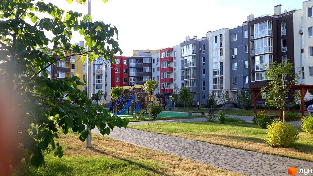 Житловий комплекс Нова Буча з яскравими фасадами та дитячим майданчиком. Сучасна архітектура та доглянута прибудинкова територія.