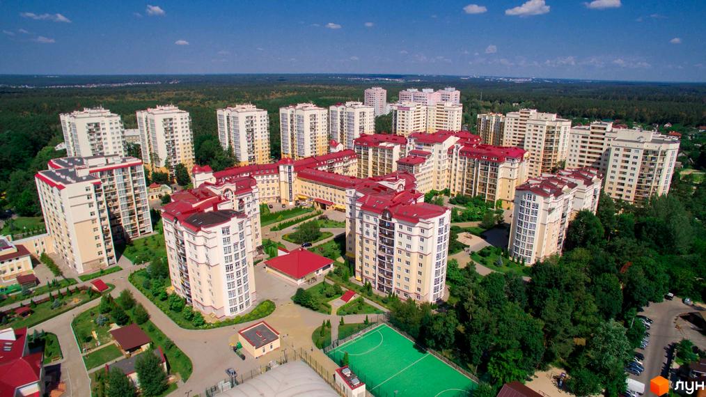 Багатоповерхові будинки Житлового комплексу Чайка з світлими фасадами та червоними дахами. Прибудинкова територія має багато зелених насаджень та спортивне поле.