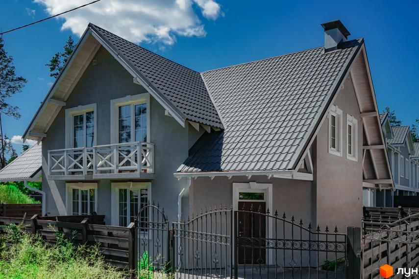 Зовнішній вигляд двоповерхового будинку з сірим дахом та білим балконом. Навколо будинку розташована огорожа та зелені насадження.
