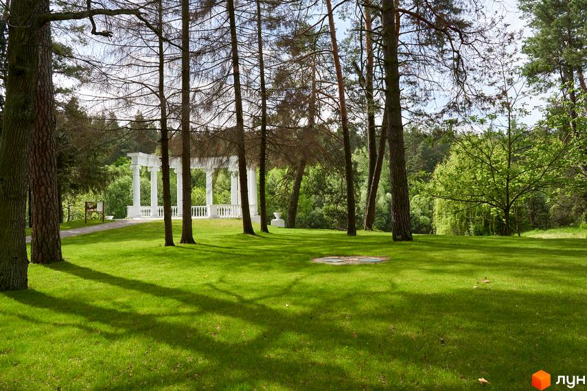 O2 Residence: біла альтанка з колонами на зеленій галявині серед дерев. Паркова зона з доглянутим газоном та тінями від дерев.