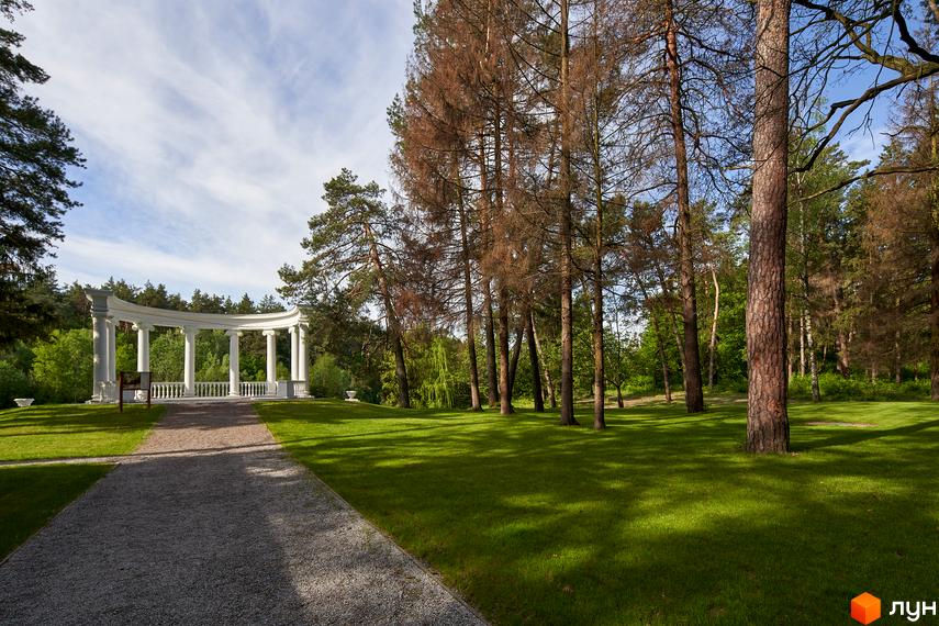 Житловий комплекс O2 Residence з білою колонадою на тлі зеленого парку та дерев. Доглянута територія з гравійною доріжкою.