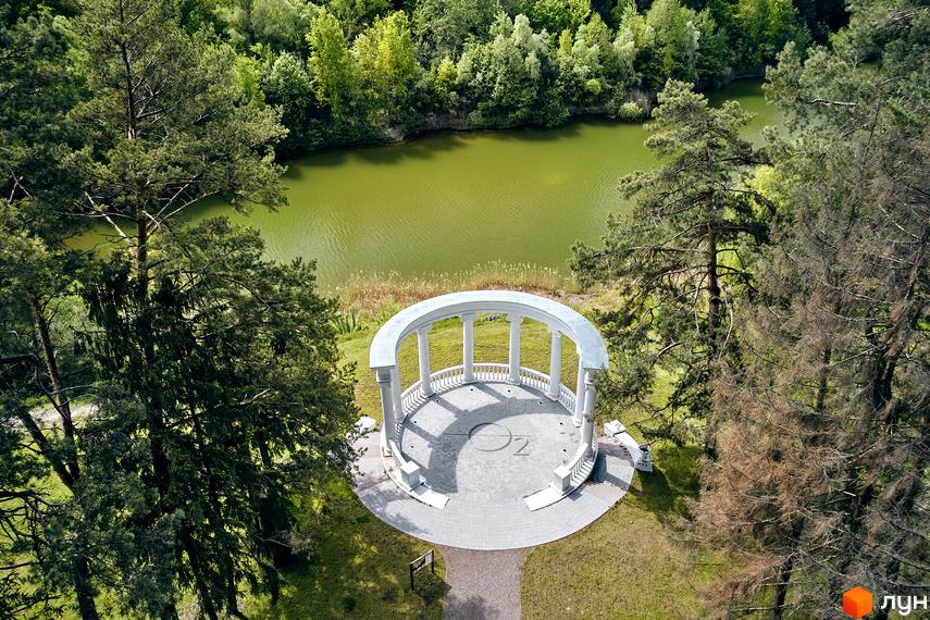 Житловий комплекс O2 Residence з білим альтанкою та озером. Навколо комплексу зелені дерева та галявини.