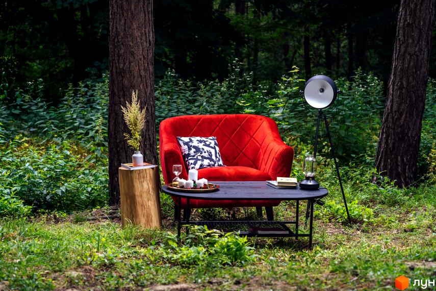 O2 Residence: затишний червоний диван у лісовій зоні біля журнального столика з декором. Навколо зелені дерева та трава.