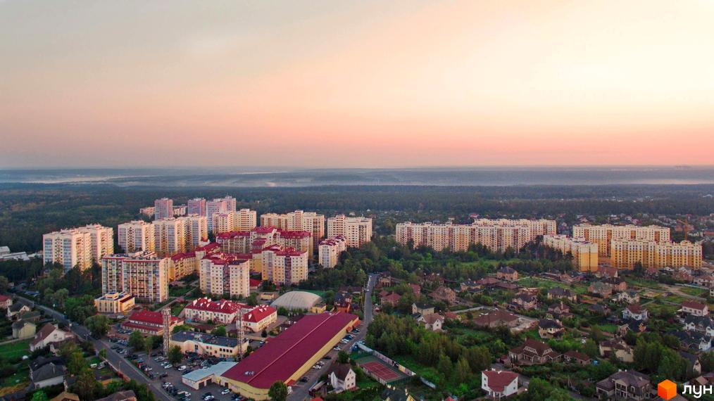 Багатоповерхові будинки Житлового комплексу Чайка з світлими фасадами та червоними дахами, розташовані серед зелених дерев, приватних будинків та лісової зони.