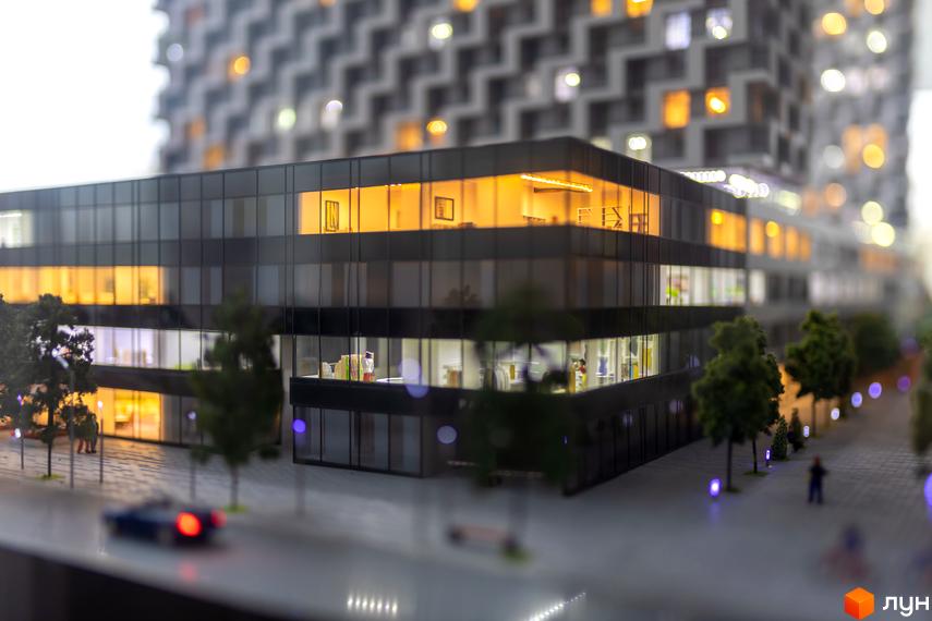 Зображення макету будинку з великими вікнами та прибудинковою територією з деревами. На задньому плані висотна будівля.