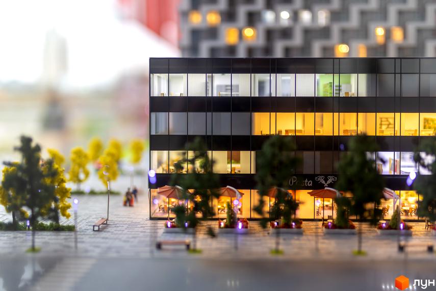 Фасад житлового комплексу BOSTON Creative House з темними вікнами та освітленими комерційними приміщеннями на першому поверсі. Прибудинкова територія з деревами, лавками та кафе.