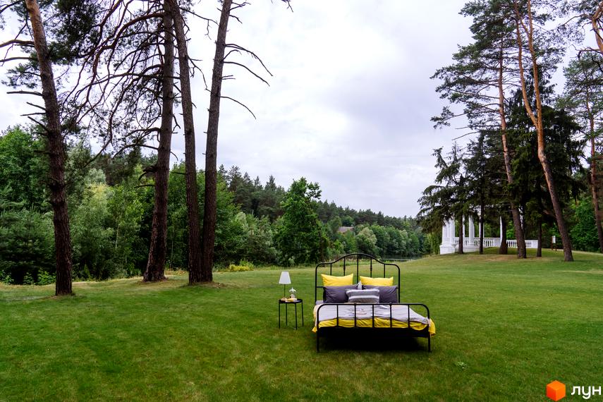 O2 Residence - житловий комплекс з ліжком та приліжковою тумбою на зеленій галявині біля лісу. На задньому плані видно білий альтанку та дерева.