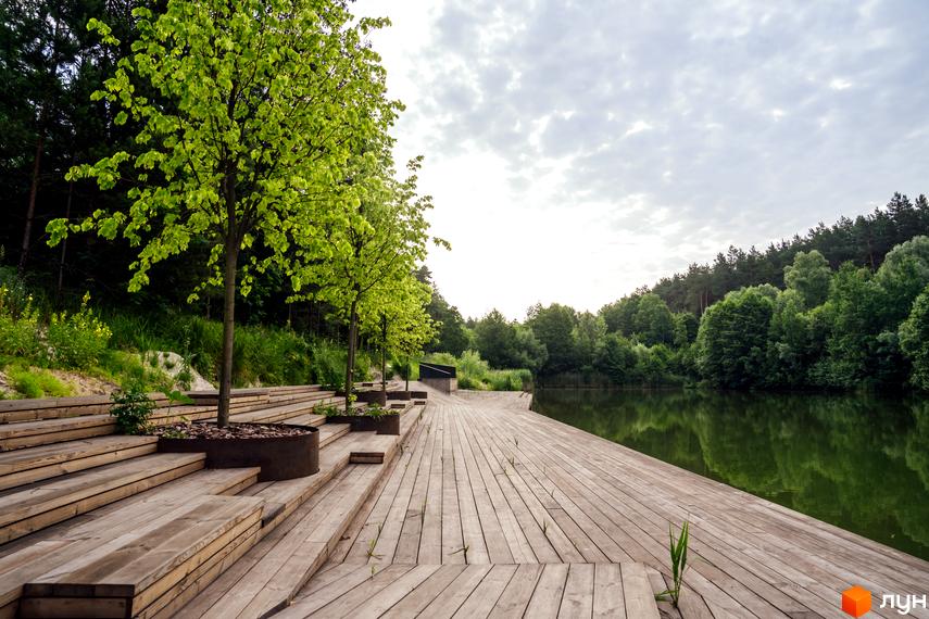 O2 Residence: дерев'яні тераси та ландшафтний дизайн біля озера. Зелені дерева та водойма створюють затишну атмосферу для відпочинку.