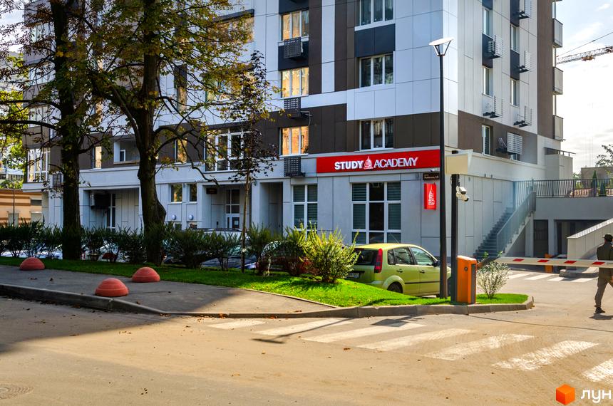 Житловий комплекс Святобор з фасадом з білих, сірих та коричневих панелей. Прибудинкова територія з деревами, кущами та дорогою з пішохідним переходом.