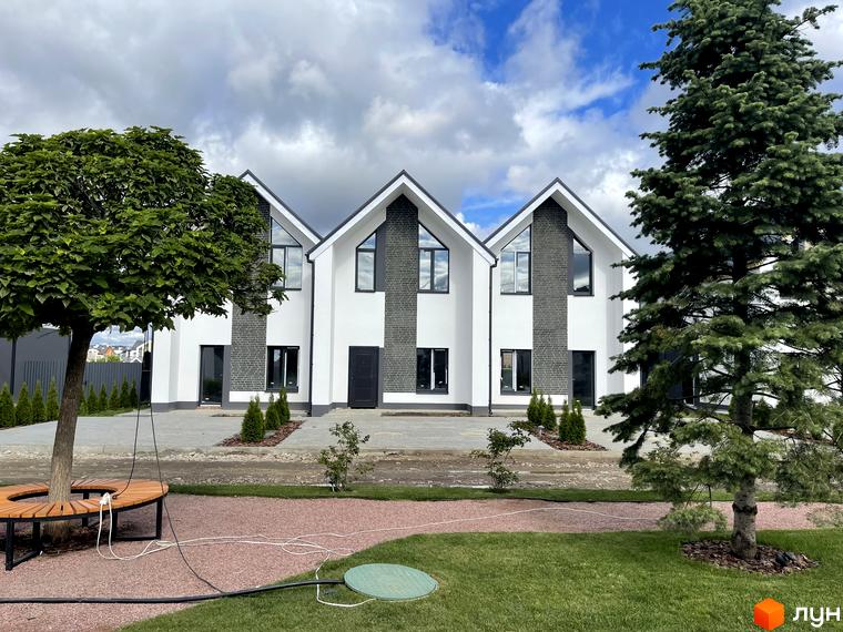 Котеджне містечко Щаслива Вулиця: три білі будинки з темними дахами та цегляними вставками. Прилегла територія має газон, доріжки та великі дерева.