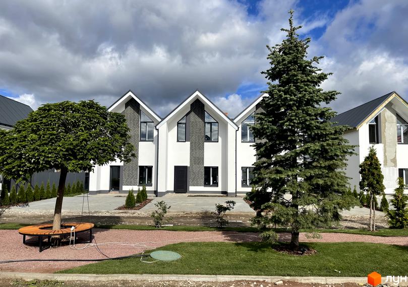 Котеджне містечко Щаслива Вулиця: двоповерхові будинки з білими фасадами та темною цеглою. Прибудинкова територія з доріжками, газонами та деревами.