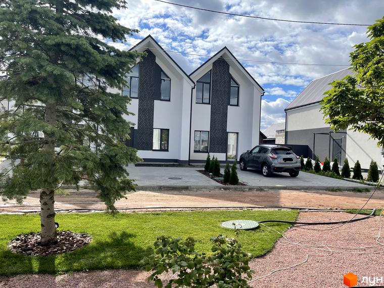 Фасад Котеджного містечка Щаслива Вулиця: два білі будинки з темними акцентами та вікнами. Прибудинкова територія з газоном, деревами та парковкою.