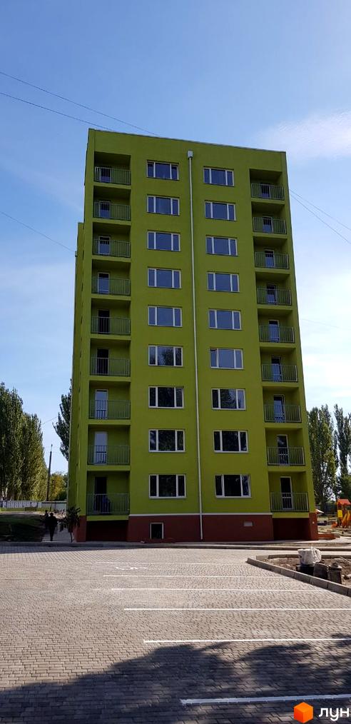 Зелений багатоповерховий будинок ЖК на Даманському з балконами та великими вікнами. На передньому плані бруківка, на задньому - дитячий майданчик.