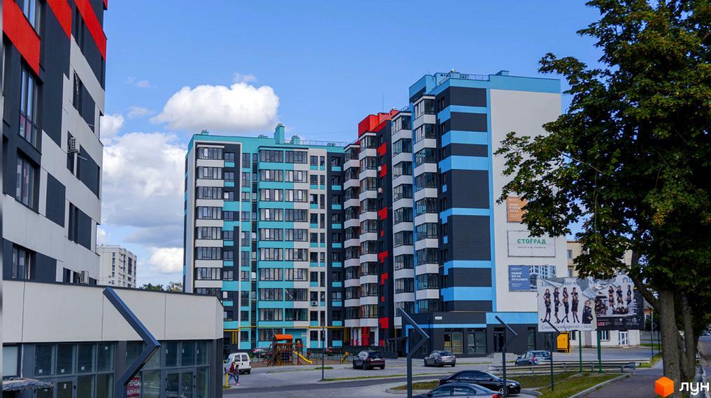 Зовнішній вигляд новобудови ЖК Bridge Town з яскравим фасадом та прибудинковою територією з дитячим майданчиком. Фотографія комплексу з машинами та деревами.