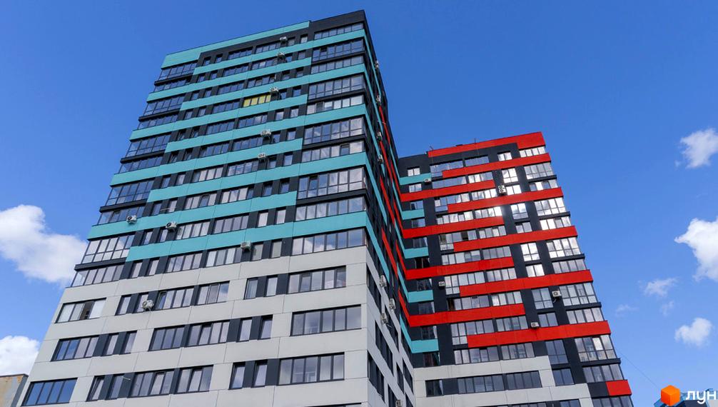 Житловий комплекс Bridge Tower – це висотна будівля з яскравими фасадами у бірюзових, червоних та сірих кольорах, що має багато вікон. Чудовий вигляд на блакитному небі.