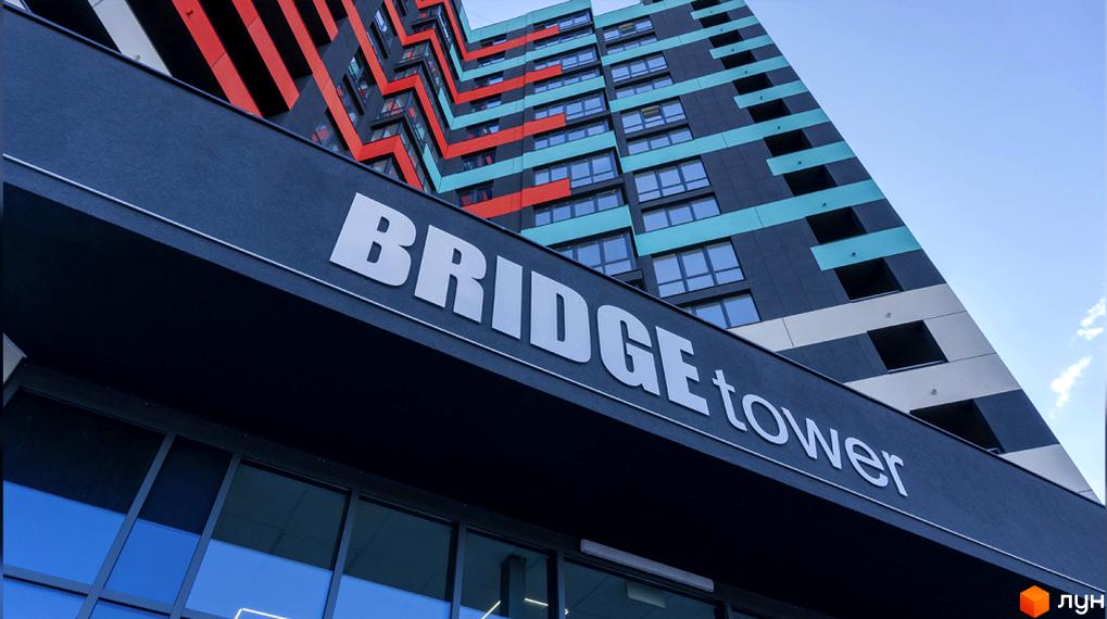 Зовнішній вигляд новобудови ЖК Bridge Tower з фасадом, оздобленим чорними, бірюзовими та червоними елементами. Сучасна архітектура будівлі.