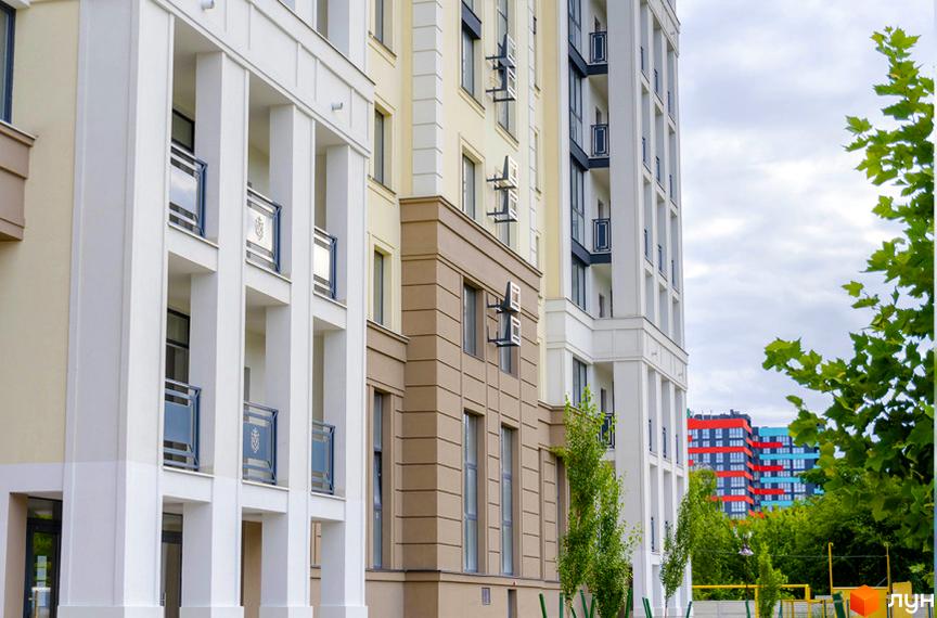 Висотна будівля житлового комплексу Prestige Apartments з білими колонами та балконами. Поруч зелені дерева та блакитне небо.
