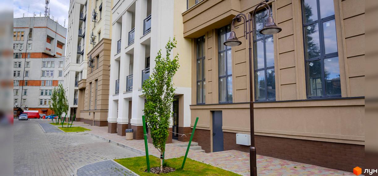 Зображення фасаду будинку ЖК Prestige Apartments. На передньому плані доглянута прибудинкова територія з деревами та бруківкою.