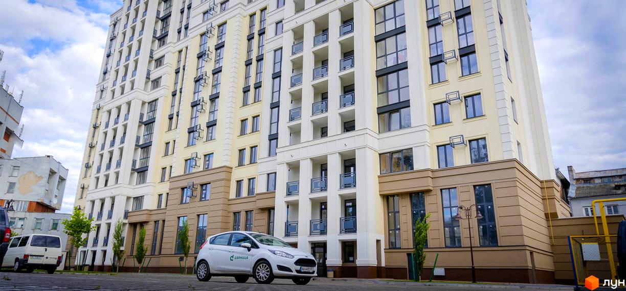 Висотна будівля ЖК Prestige Apartments з великою кількістю вікон та балконів. Біля будинку припаркований автомобіль, висаджені дерева.
